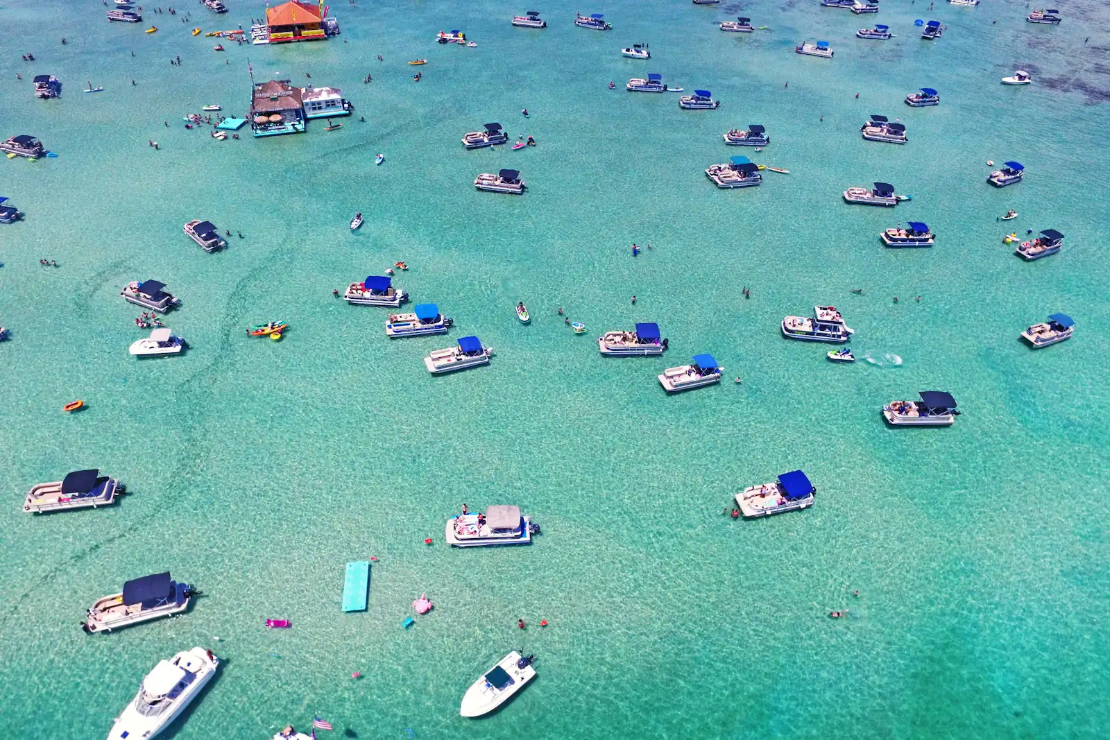 Aerial view of dozens of small boats anchored together over a pale shallow sandbar