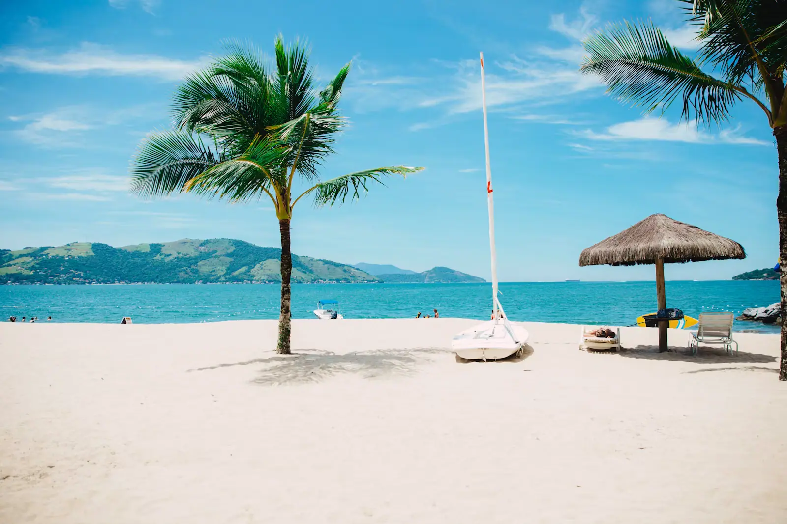 People standing waist deep on a bright sand flat with a small boat moored beyond them