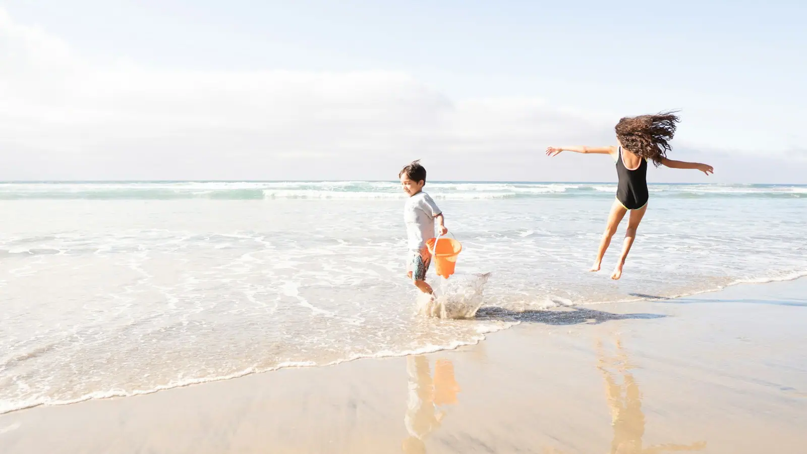 Two children running along wet sand at the edge of shallow water