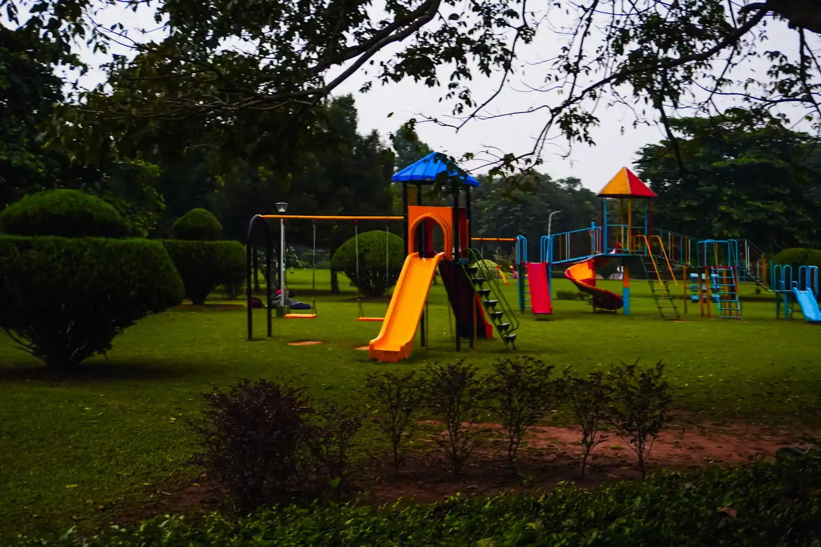 A colourful playground with slides and climbing frames set on mown grass between trees