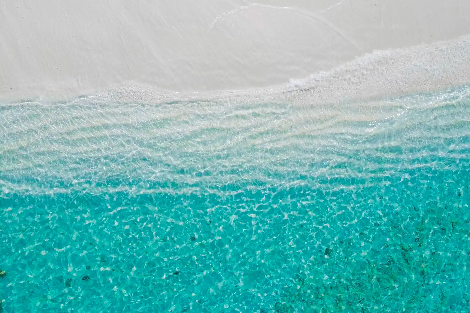 Aerial view of bright white sand meeting shallow water that shades from pale green to deep blue