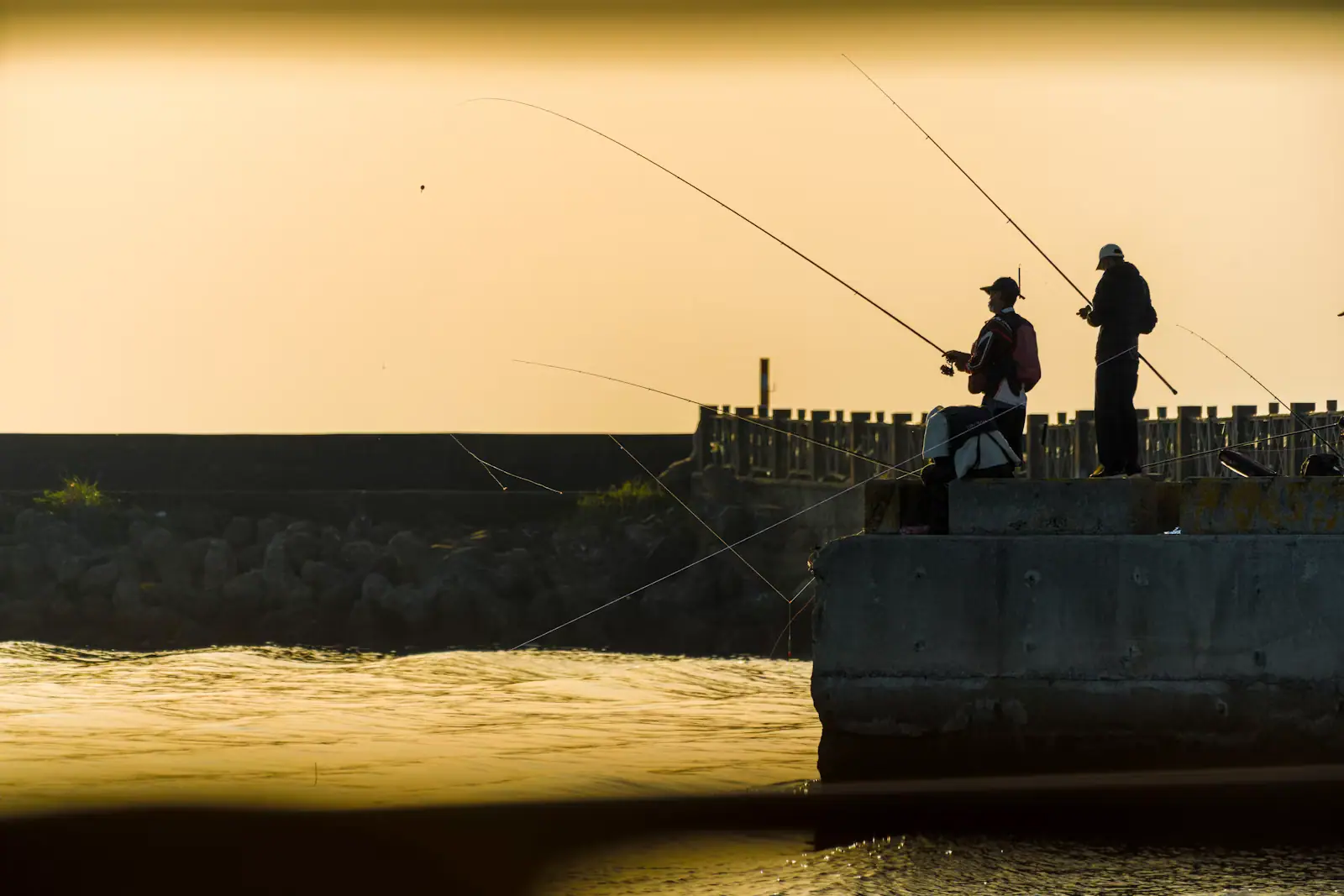 Two anglers casting from a concrete pier into open water in the last light of the evening