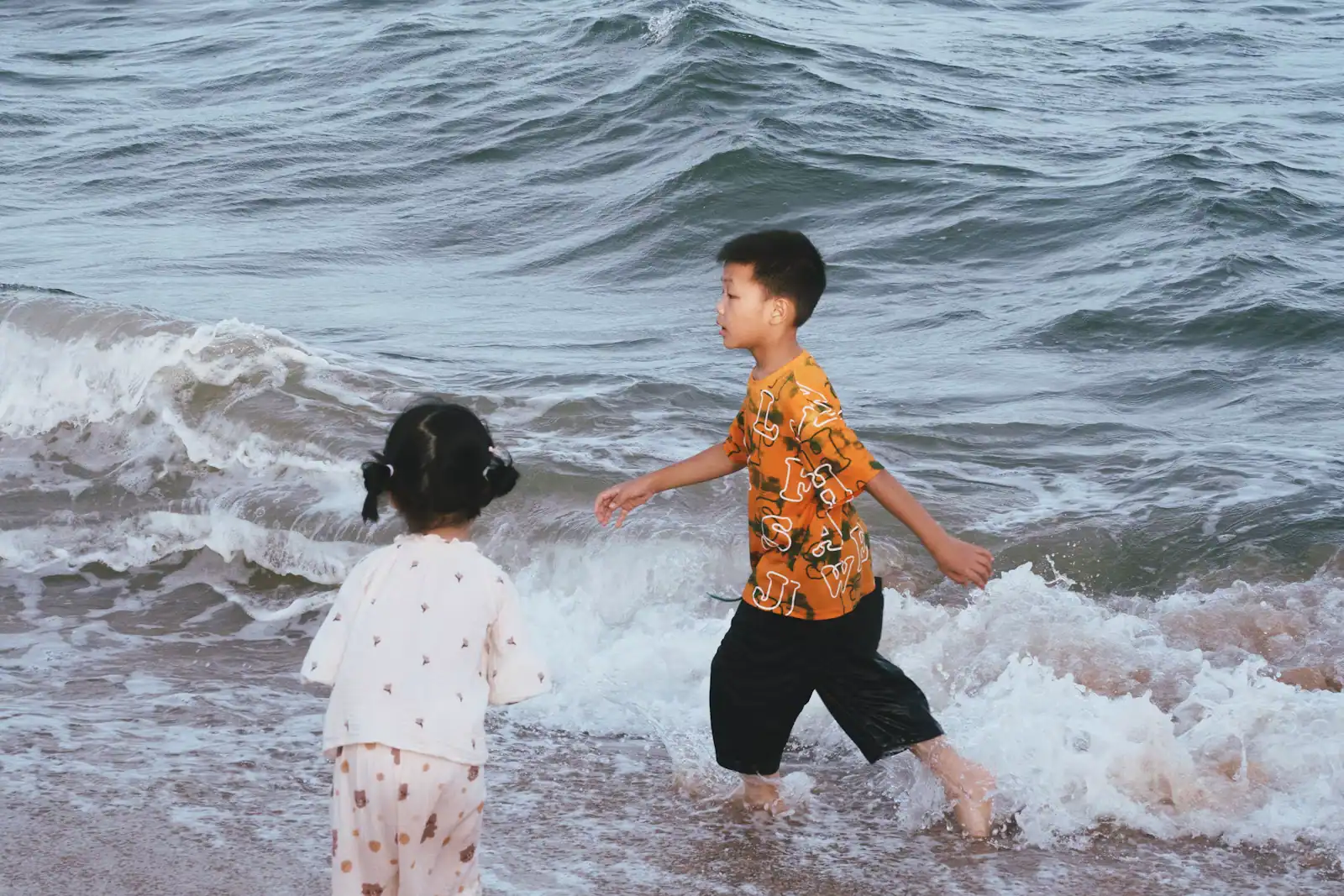 Two children playing in shallow water at the edge of a sandy beach