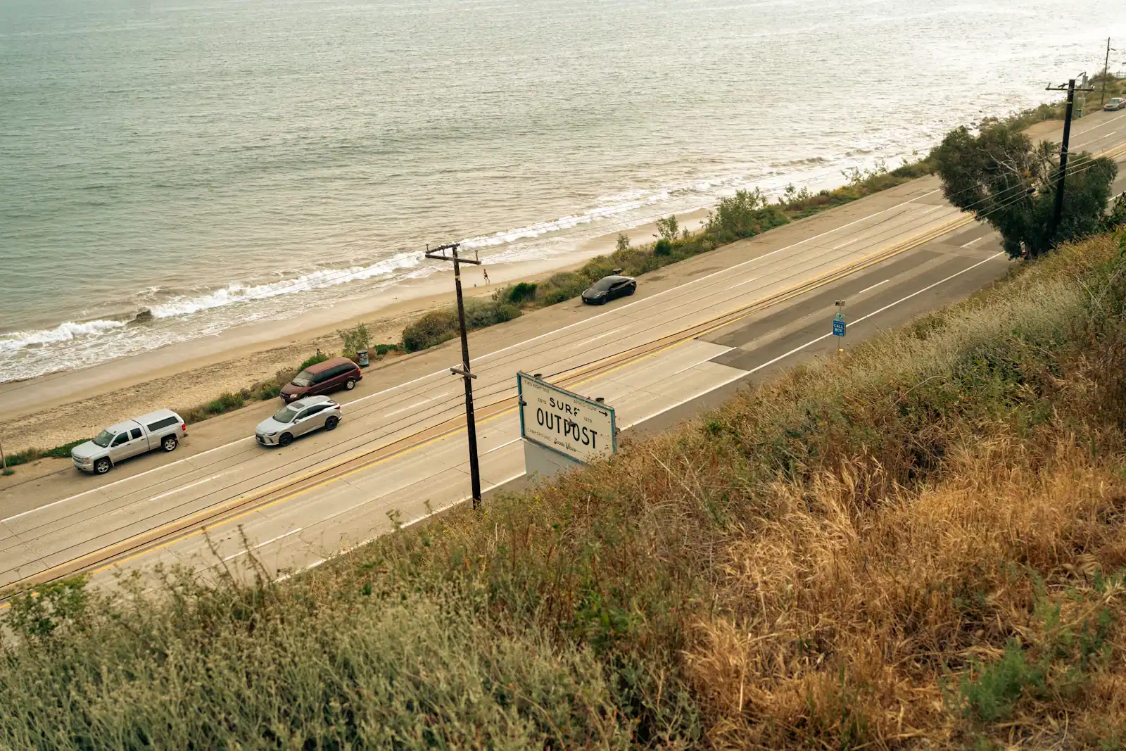 Cars moving along a two-lane coastal highway with open water alongside it