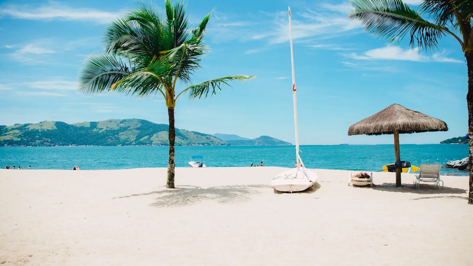 People standing waist deep on a bright sand flat with a small boat moored beyond them