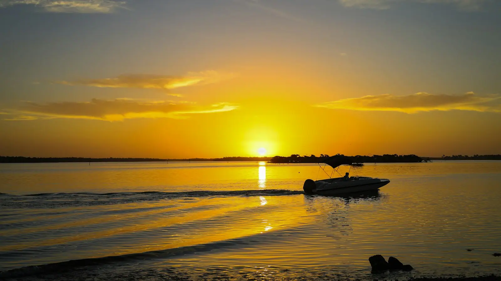 The sun low over open water with a small boat silhouetted against the light