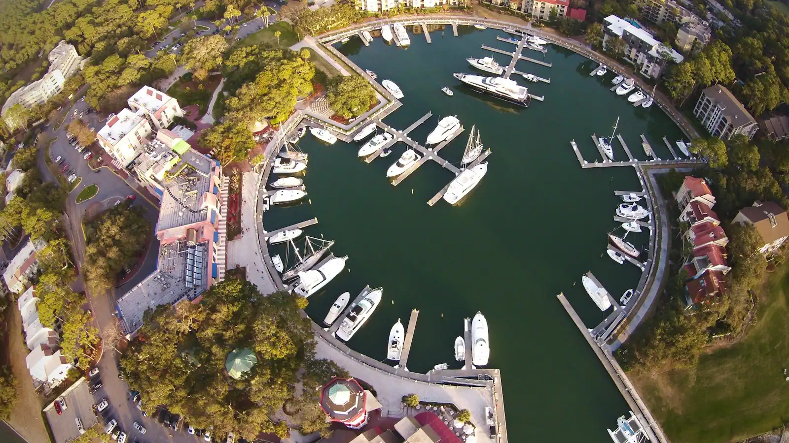 An aerial view of a marina basin ringed by docks, moored boats and low waterfront buildings